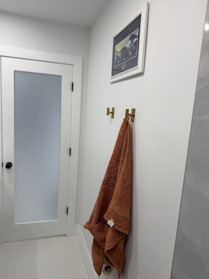 A bathroom with a white door, a towel rack with a brown towel, and a framed picture on the wall.