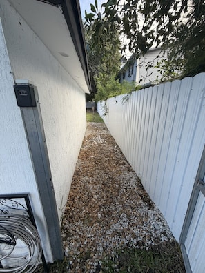 A narrow pathway with gravel, a white fence, and a metal gate.