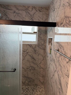 A bathroom with marble walls, a shower area, and a window.