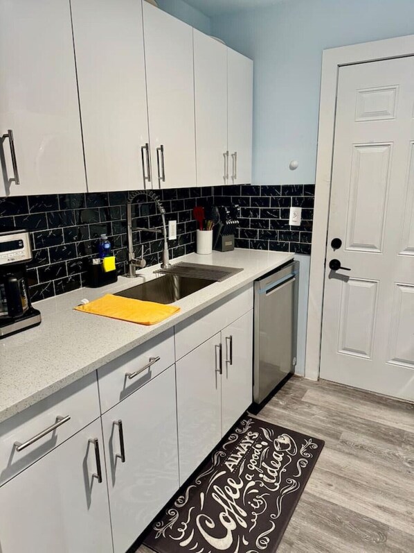A kitchen with white cabinets, a black and white tiled backsplash, a stainless steel sink, and a yellow towel on the counter.
