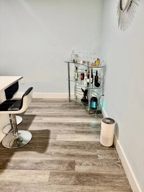 Ein Zimmer mit Holzboden, einem weißen Stuhl, einer Glasablage mit Flaschen und einer weißen Wand.