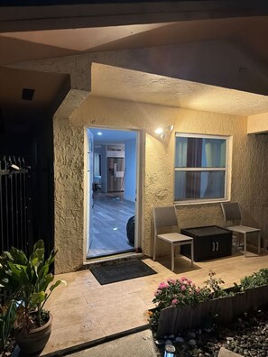 A stone exterior with a door leading to an interior space, a small outdoor seating area, and a window with curtains.