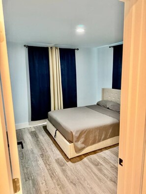 A bedroom with a bed, curtains, and a wooden floor.