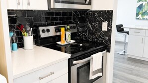 Une cuisine avec des armoires blanches, un dosseret en marbre noir et blanc, une cuisinière en acier inoxydable et un four à micro-ondes placé au-dessus.