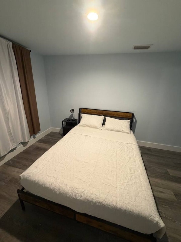 Ein Schlafzimmer mit einem Bett, einem Nachttisch, einer Lampe und einem Fenster mit VorhÀngen.