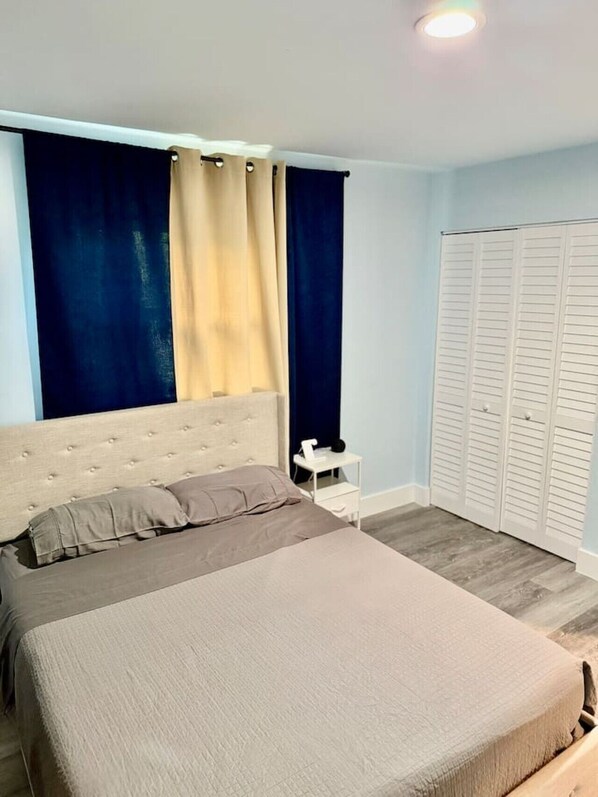 A bedroom with a bed, a nightstand, a wardrobe, and a window with curtains.