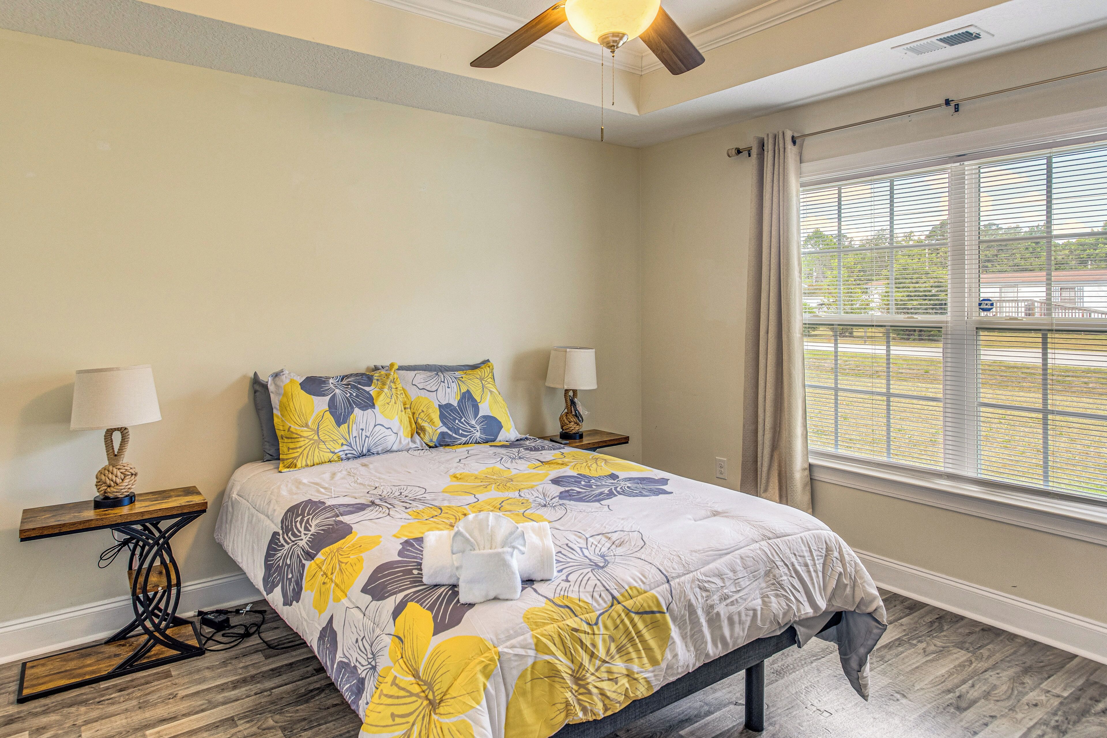 A bedroom with a bed, two bedside tables, a ceiling fan, and a window with curtains.