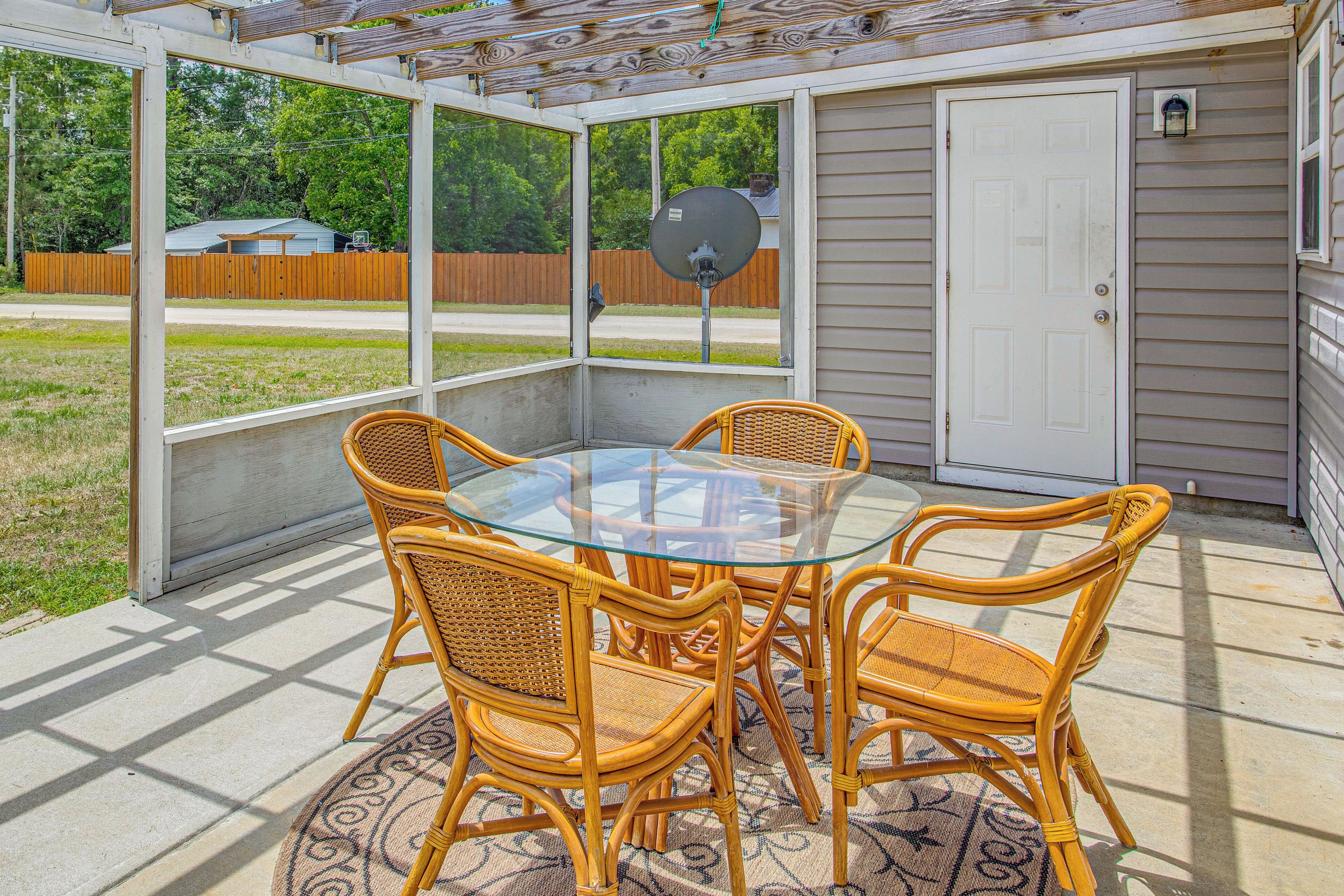 A covered patio with a glass table and wicker chairs, a door, and a satellite dish.
