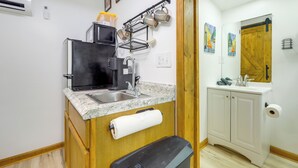A compact kitchen with a built-in refrigerator, a coffee maker, a sink, and a roll of toilet paper.