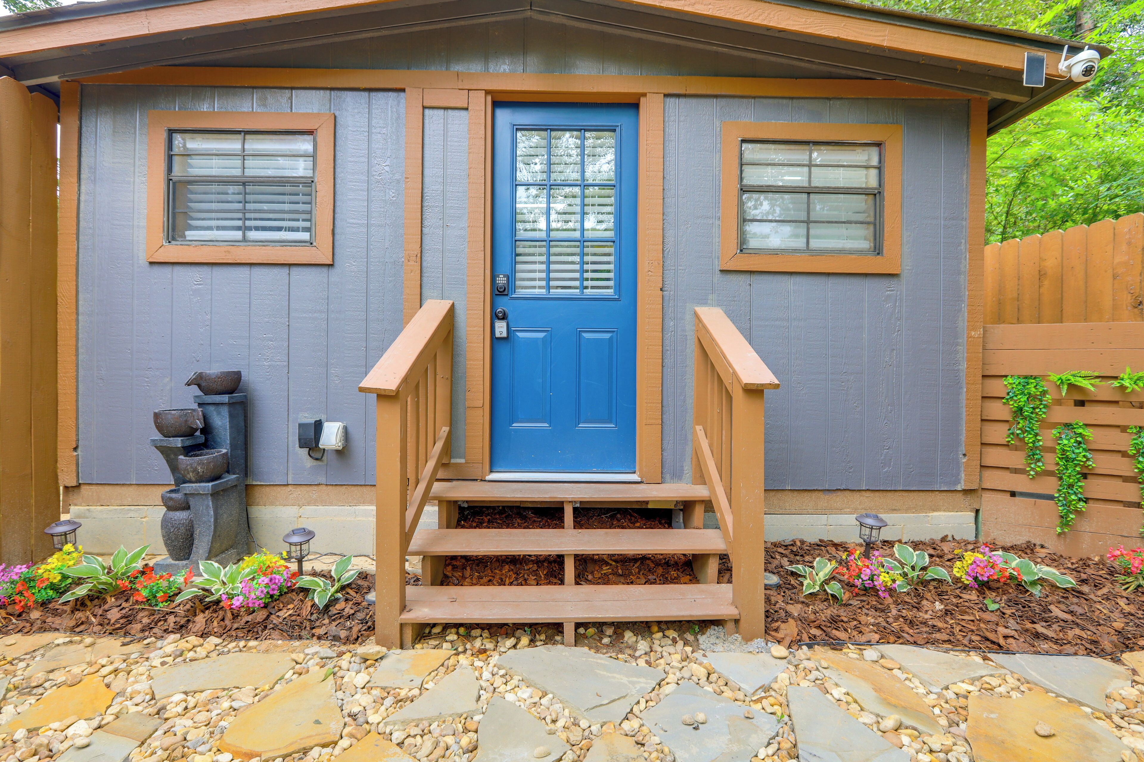 Une maison avec une porte d’entrée bleue, deux fenêtres, un escalier en bois et un chemin en pierre.