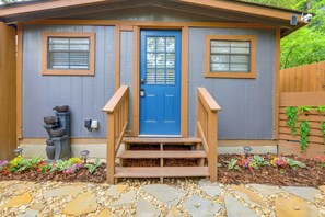 Una casa con puerta azul, dos ventanas, una escalera de madera y un camino de piedra.