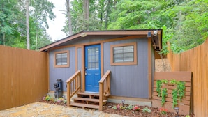 A small wooden cabin with a blue door, a wooden staircase, and a garden area with stepping stones and plants.