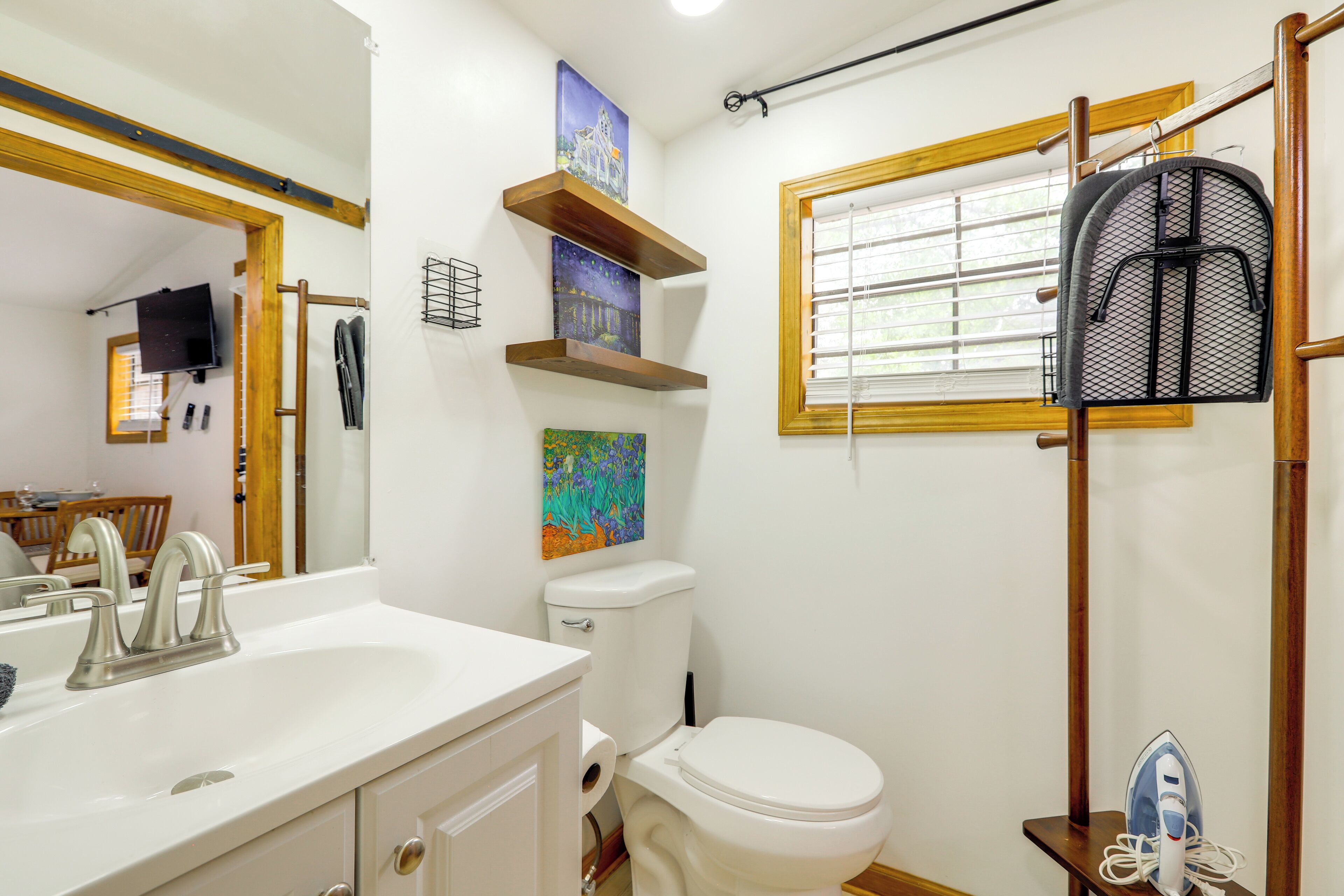 A bathroom with a white sink, toilet, and a shower area with a wooden frame and a window.