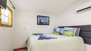 A bedroom with a bed, a painting, and an air conditioner.