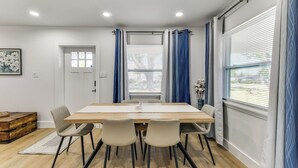 A dining area with a wooden table, four chairs, a vase with flowers, and a window with blinds. - Work & Play in Palmetto! Pet-friendly Home w/ Yard (Palmetto)