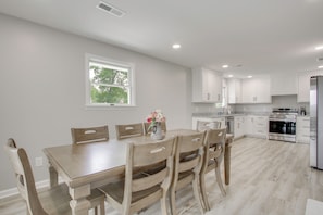 A modern kitchen with white cabinets, a wooden dining table, and a built-in oven.