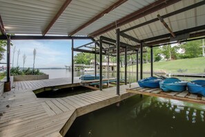 A covered dock area with boats, a wooden deck, and a view of a house and trees across the water. - Private Dock! Fishing Paradise on Lake Wilson (Killen)
