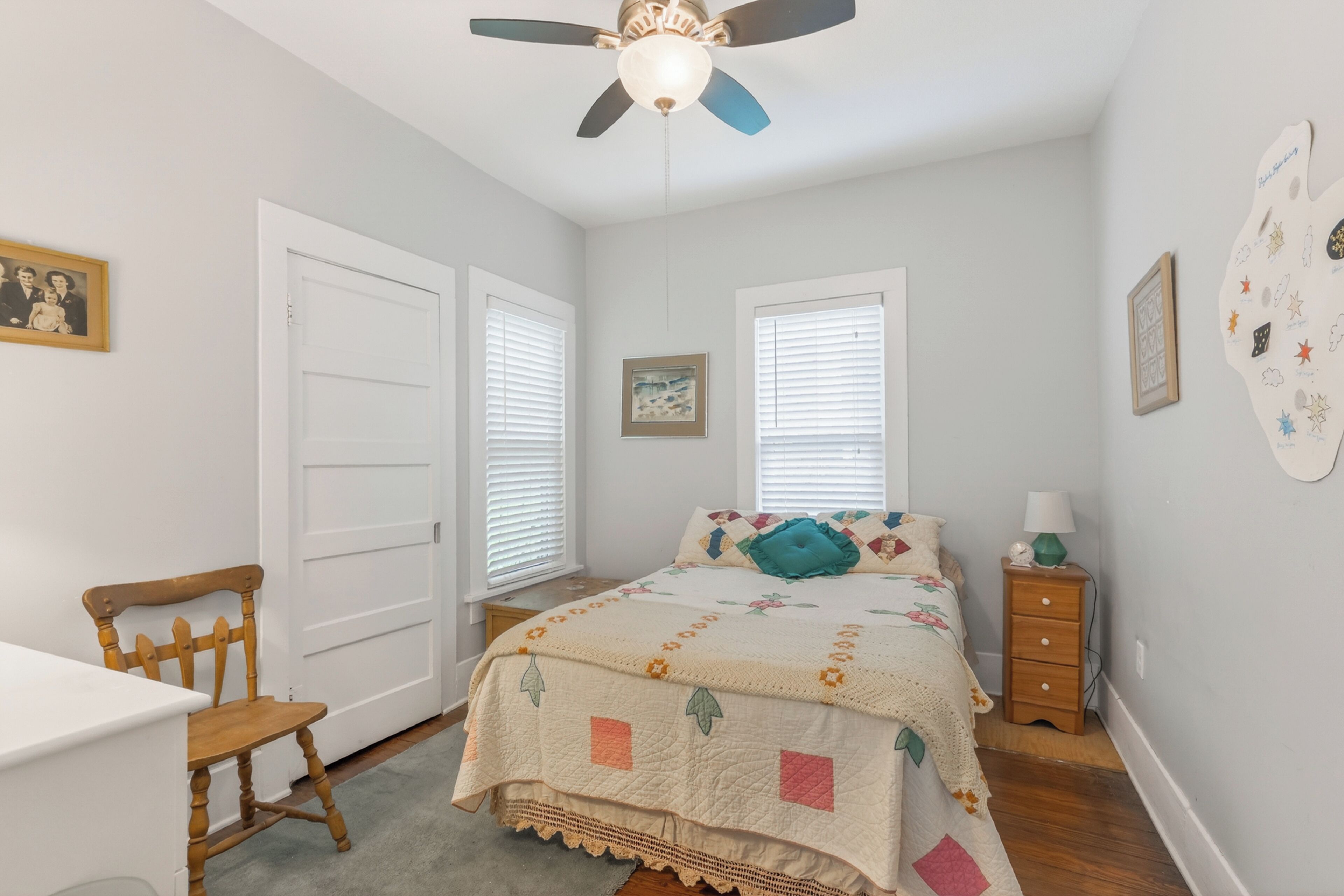 A bedroom with a bed, a chair, a desk, a ceiling fan, and a wall with a decorative plate.