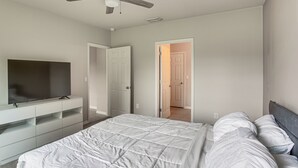 Een slaapkamer met een bed, een televisie op een standaard en een plafondventilator.