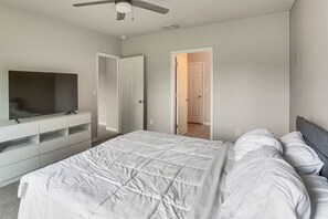 A bedroom with a bed, a TV on a stand, and a ceiling fan.