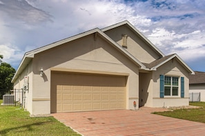 A residential house with a garage, a brick driveway, and a small lawn.