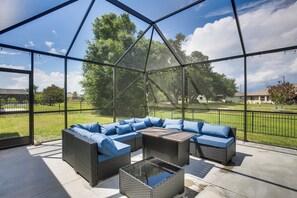 A covered patio with wicker furniture, a glass coffee table, and a view of a park.