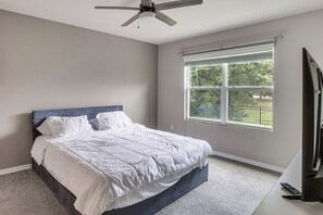 A bedroom with a bed, a ceiling fan, a window, and a TV.