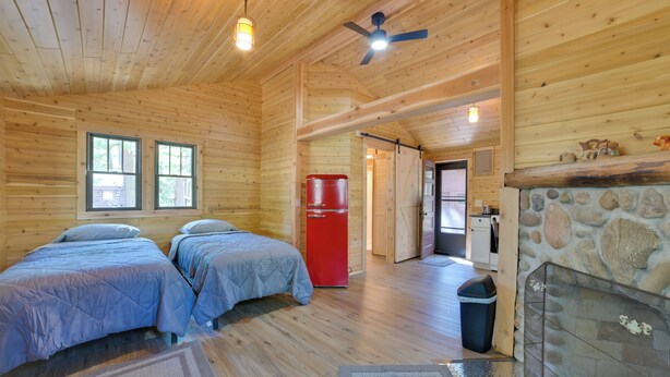 A wooden cabin with two beds, a red refrigerator, a stone fireplace, and a ceiling fan. - Nature Lover's Getaway: Studio by Pigeon River (Vanderbilt)