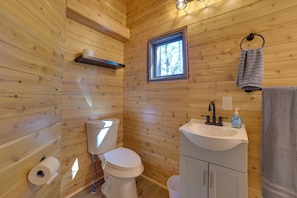 A wooden cabin bathroom with a toilet, sink, and window.