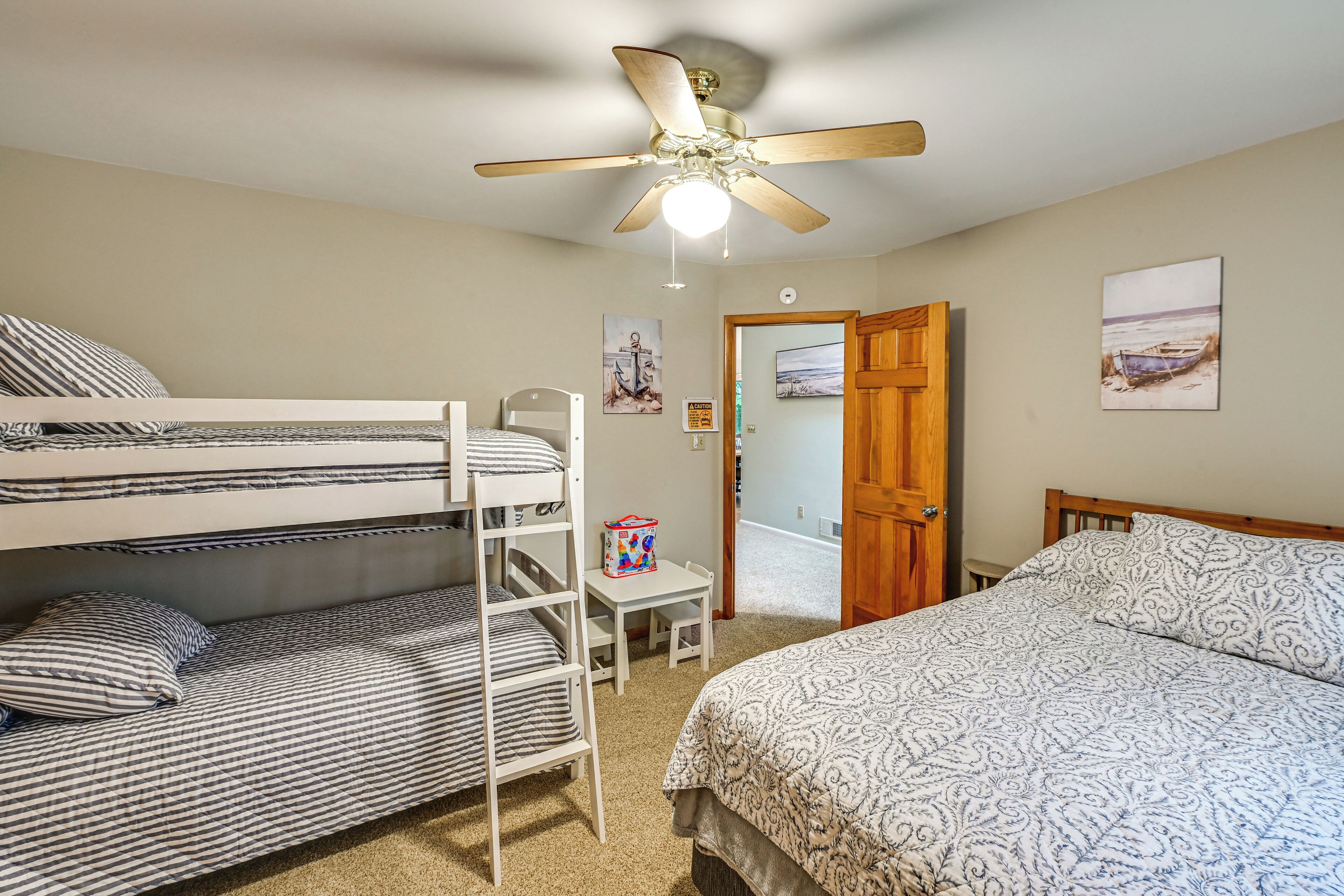 A bedroom with bunk beds, a ceiling fan, a wooden door, and a beach-themed wall art.