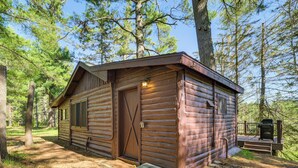 Eine Blockhütte mit Holztür, einer kleinen Veranda und einem Grill vor der Tür.