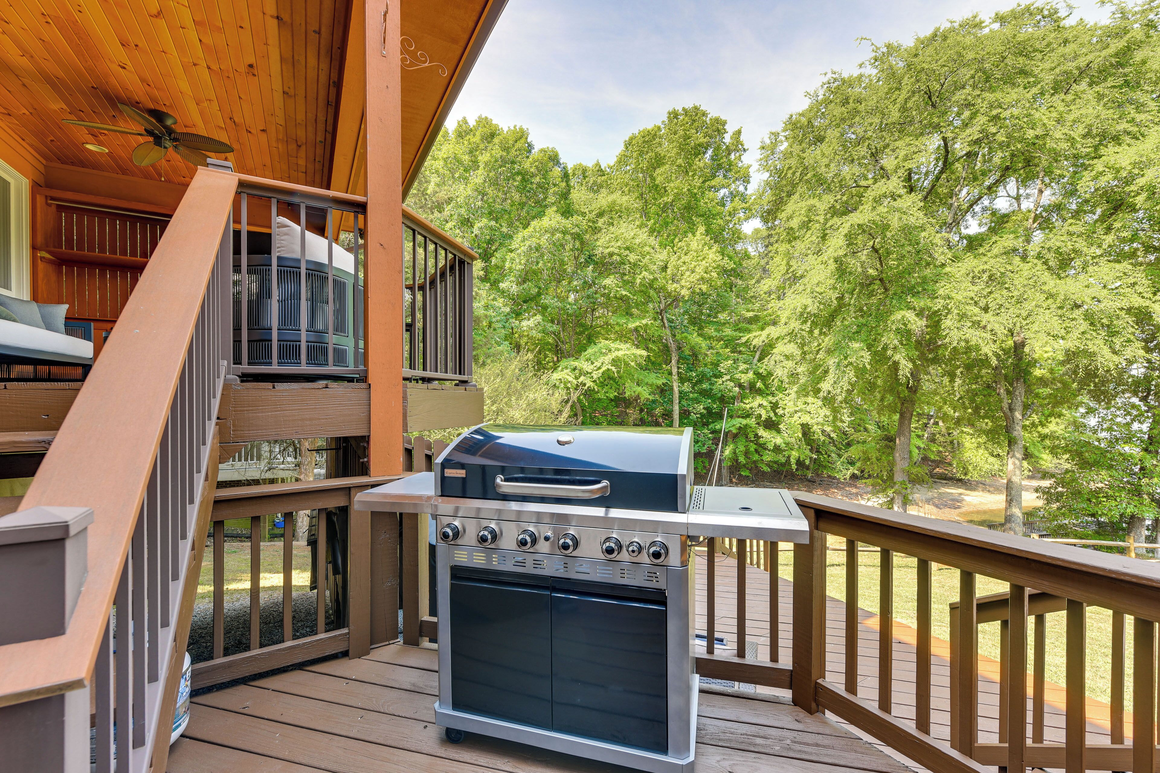 A wooden deck with a barbecue grill, a staircase, and a view of a forest.