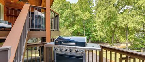 A wooden deck with a barbecue grill, a staircase, and a view of a forest.