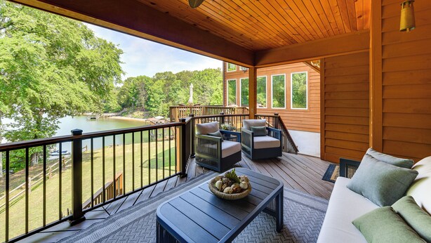 Eine Holzterrasse mit Gartenmöbeln, Blick auf einen See und einer Bootsanlegestelle.