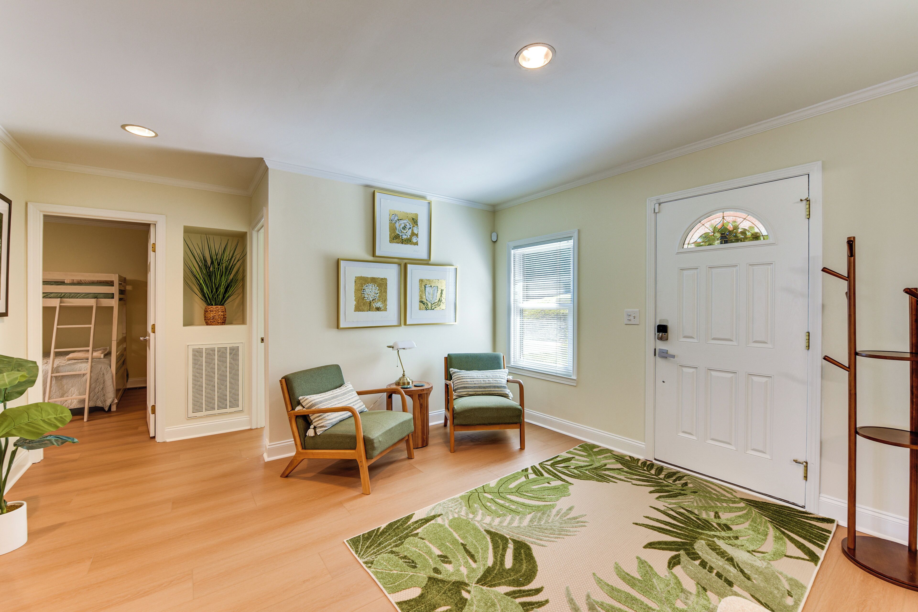 A room with a wooden floor, two chairs, a small table, a door with a window, and a plant.