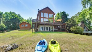 Ein großes, zweistöckiges Haus mit einer Terrasse, eine kleine Holzhütte und zwei Kajaks auf einer grünen Wiese.