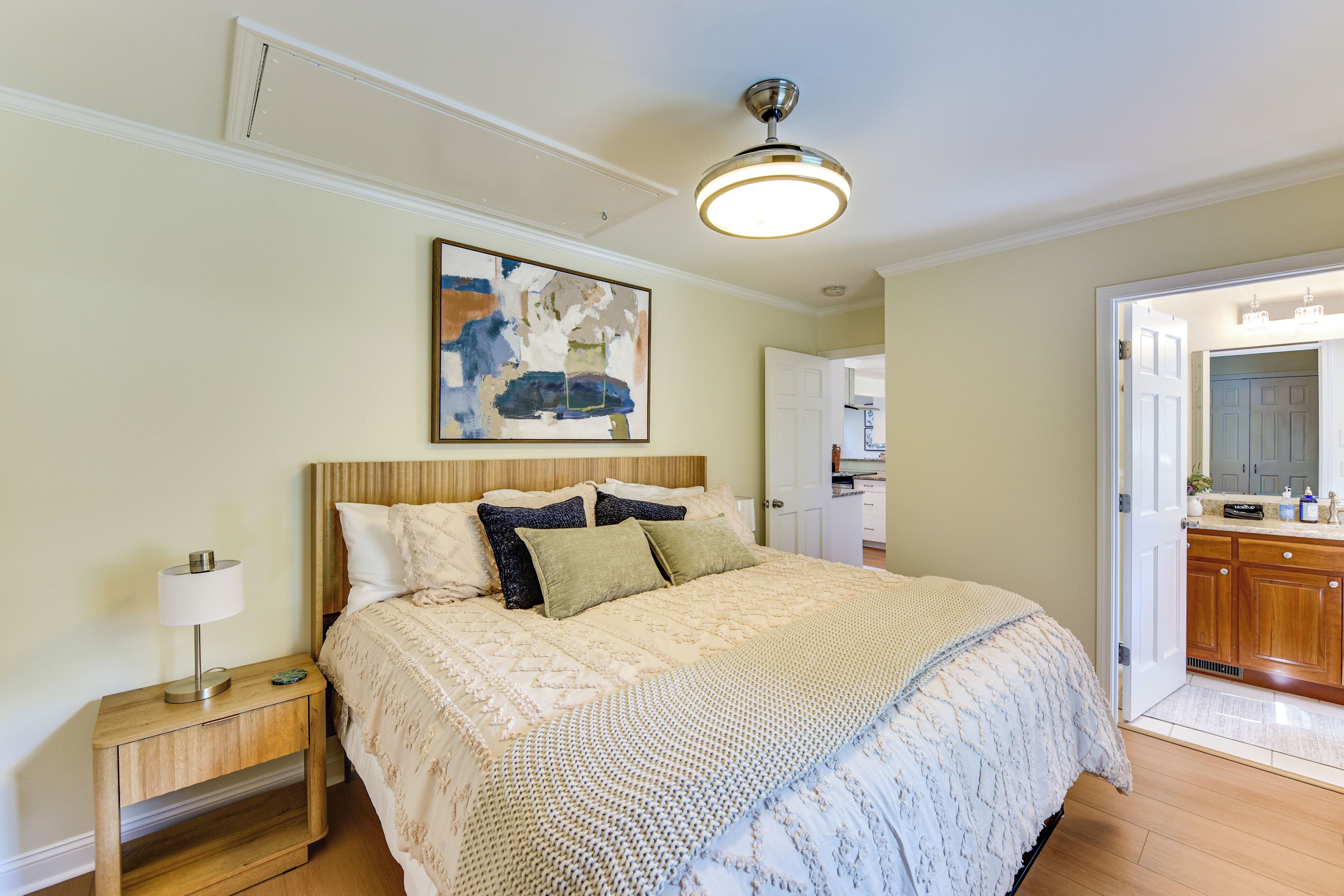 Quarto com cama, mesa de cabeceira, abajur e um quadro na parede.