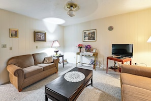 A living room with a brown sofa, a wooden coffee table, a TV stand, and framed pictures on the wall.