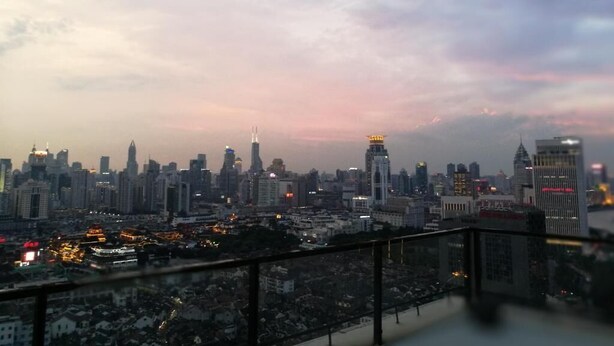 Une vue d’une ville au crépuscule, avec différents types de bâtiments, dont un gratte-ciel imposant surmonté d’une flèche.