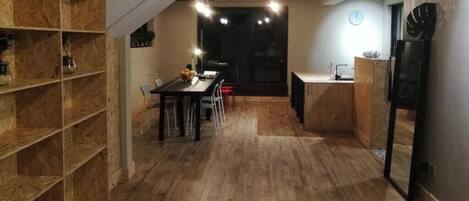 A modern kitchen with a dining area, wooden flooring, built-in shelving, and a central air conditioning unit.
