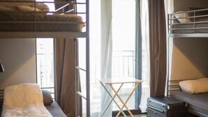 Une chambre avec des lits superposés, une petite table, une valise et une fenêtre avec des rideaux.