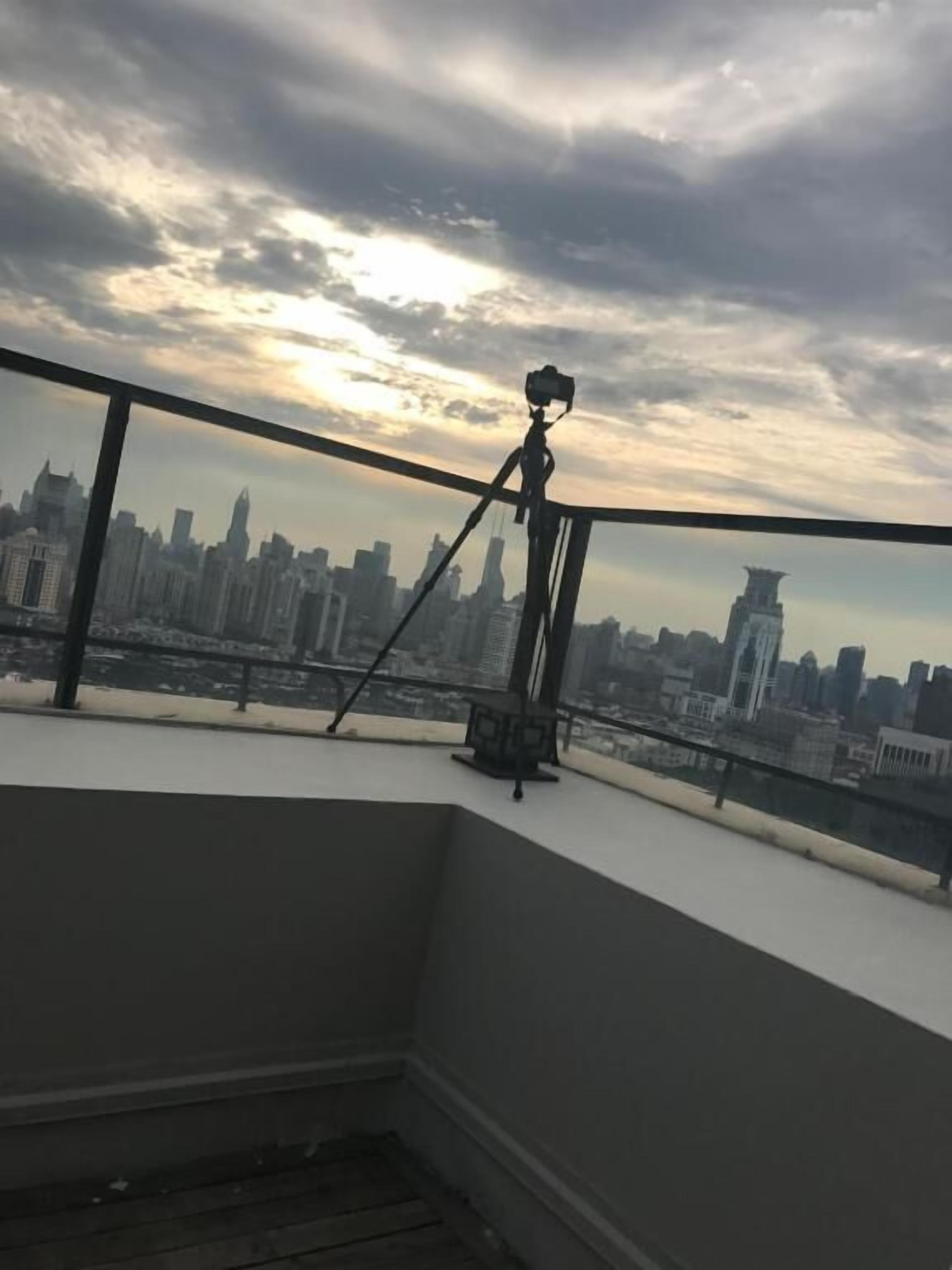 A balcony with a camera on a tripod overlooking a city skyline.
