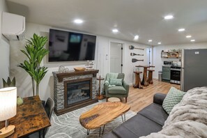 A living room with a fireplace, a TV, a sofa, a dining table, and a kitchen area. - Hot Tub, Deck! Tiny Home Retreat By Kentucky Lake (Springville)