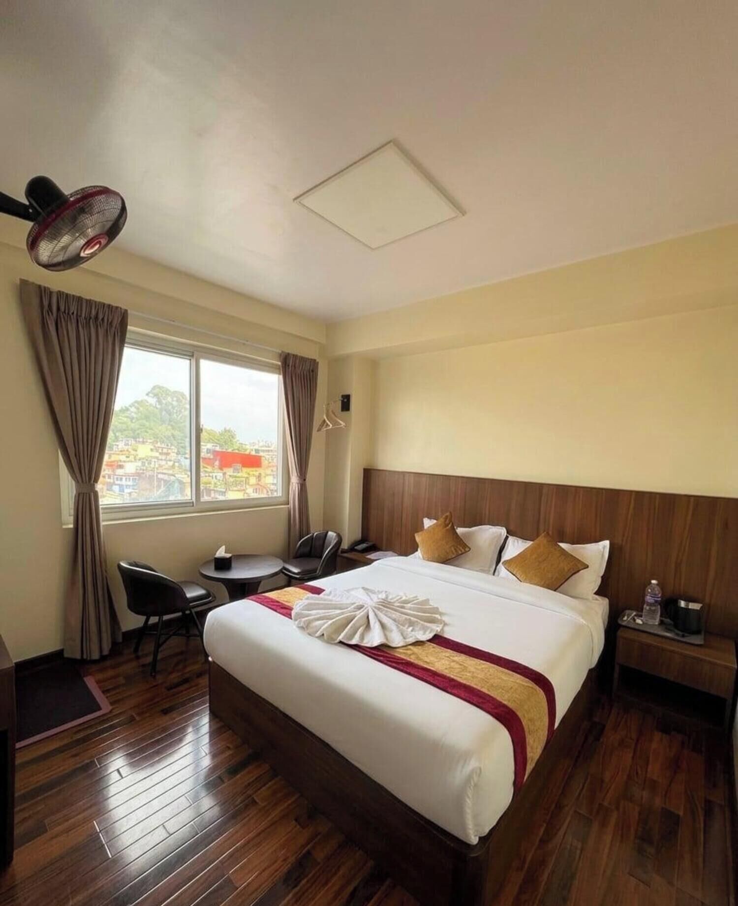A hotel room with a bed, bedside table, chair, desk, and a window with curtains.
