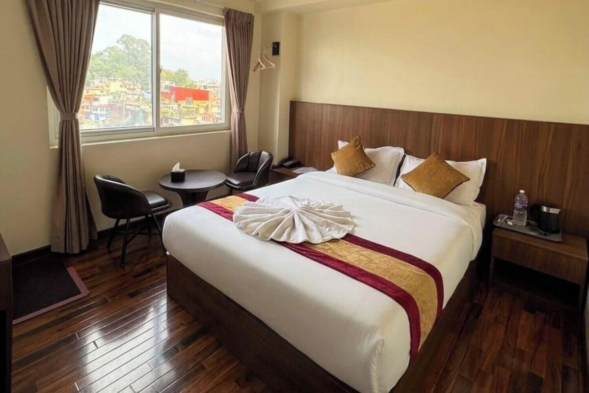 Habitación de hotel con cama, mesita de noche, silla, escritorio y ventana con cortinas.