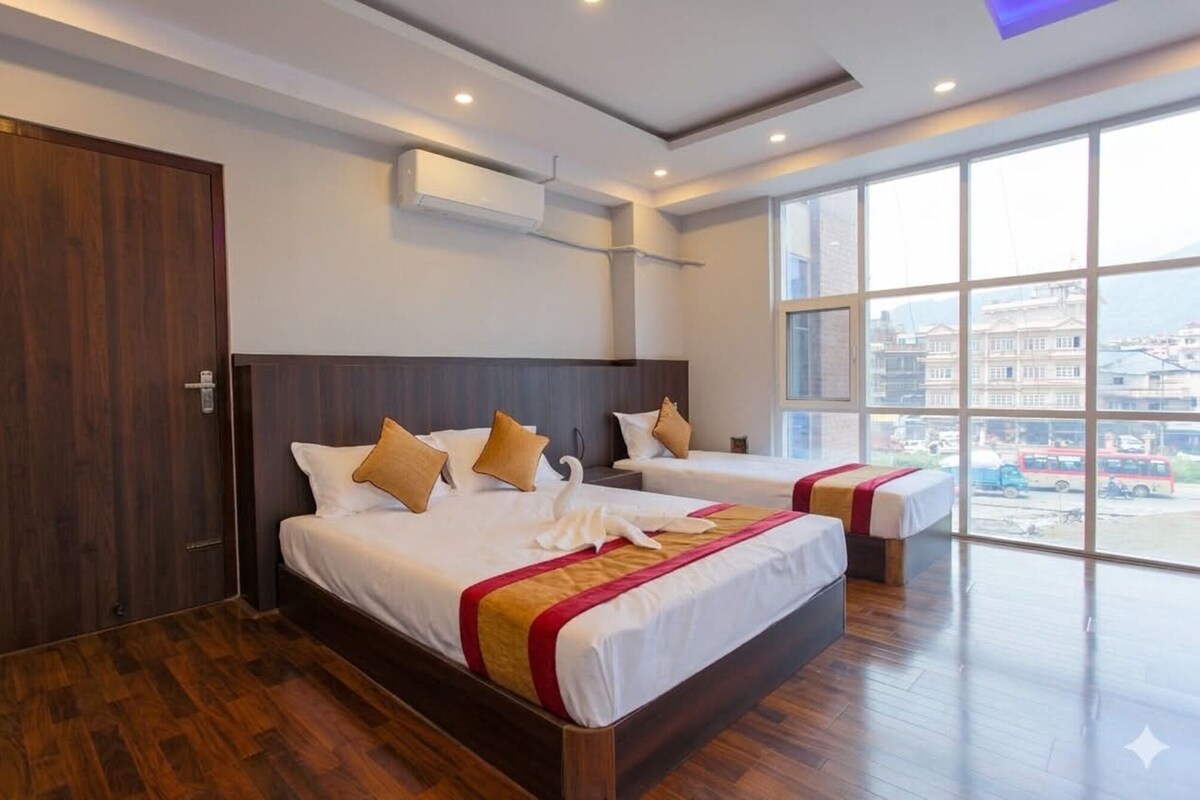 Habitación de hotel con dos camas, un ventanal grande y vistas a la ciudad.