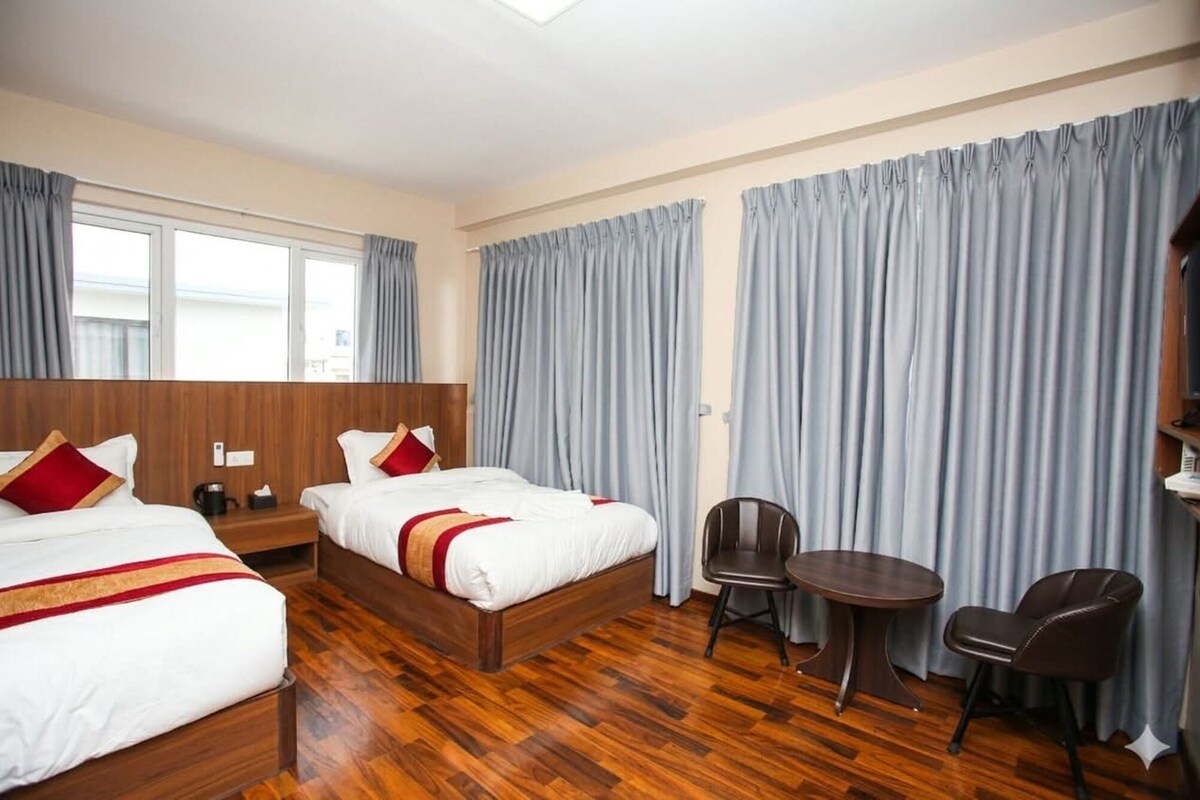 Habitación de hotel con dos camas, una mesita, dos sillas y un ventanal grande.