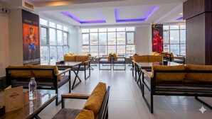 En modern hotellobby med sittgrupper, stora fönster och utsikt över staden.