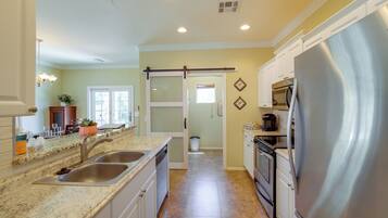 A kitchen with a stainless steel refrigerator, double sink, and a sliding door leading to another room.