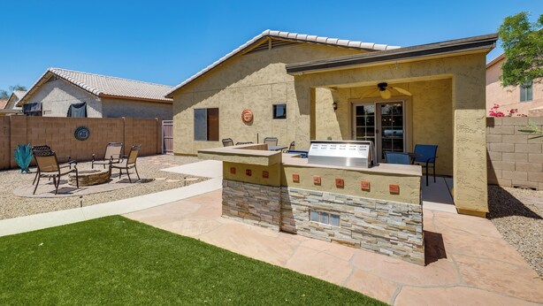 A patio with a stone barbecue and seating area, a stone wall, and a clear blue sky. - San Tan Valley Home w/ Patio in Johnson Ranch! (San Tan Valley)